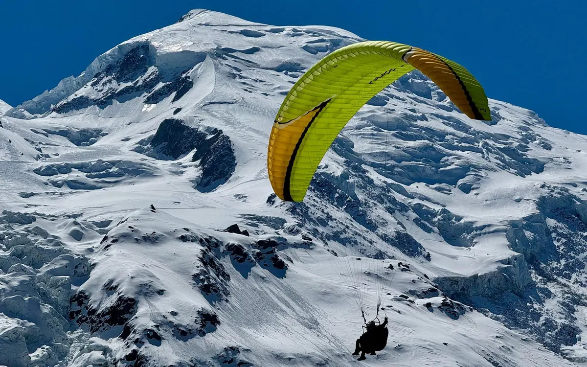 Un'ala da parapendio con pilota e passeggero in volo sopra un'ampia parete innevata
