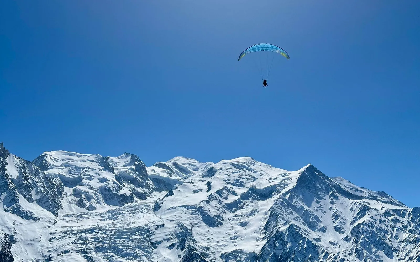 Un parapendio solitario in alto nel cielo blu intenso sopra il massiccio del Mont Blanc innevato