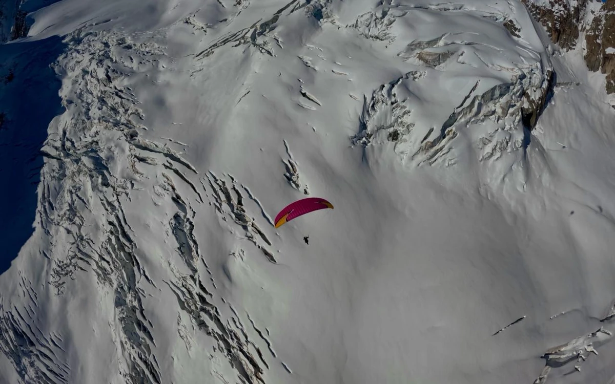 Un'ala da parapendio in volo sopra un ghiacciaio crepacciato, fotografata dall'alto