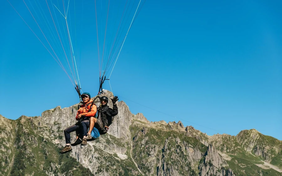 Un pilota e un passeggero seduti in un'imbracatura tandem in volo sopra cime rocciose grigie