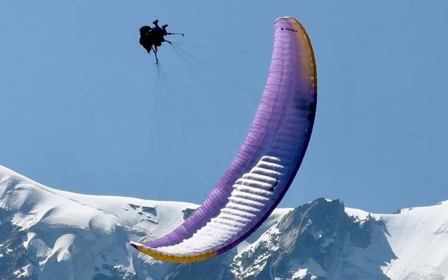 Una vela viola e bianca in volo sopra un campo di neve con cime scure sotto