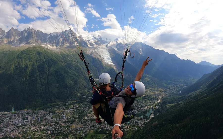 Una coppia in tandem in volo con un braccio alzato, la valle di Chamonix molto più in basso