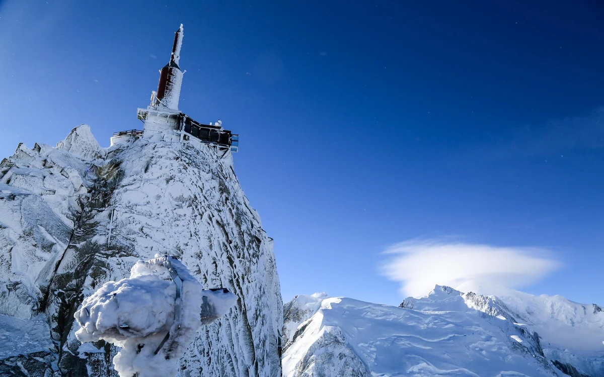 Una guglia di granito con una stazione di montagna in cima, una cresta innevata e un cielo limpido