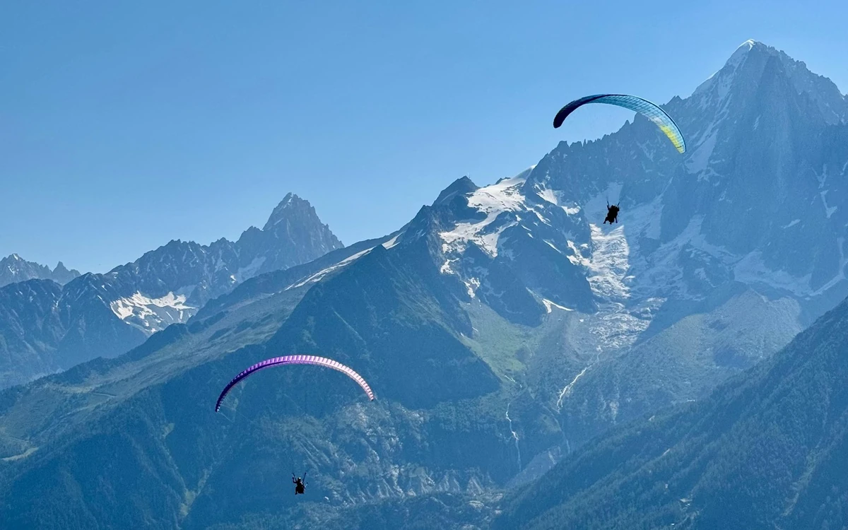 Due vele da parapendio in volo davanti a una cima rocciosa e appuntita con neve